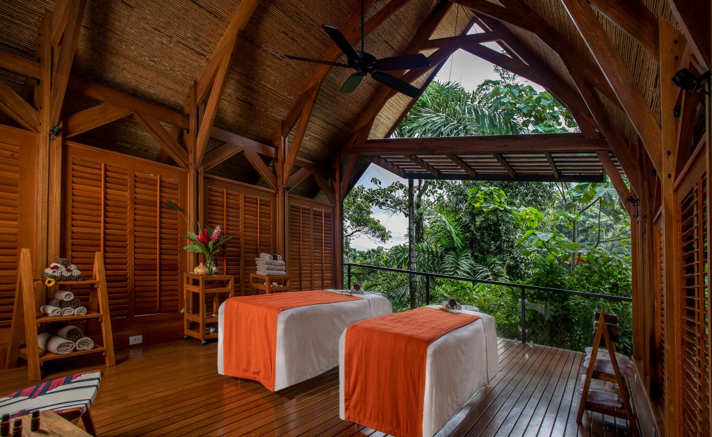 A tranquil, open-air spa treatment room with two massage tables and a direct, panoramic view of the green tropical forest.