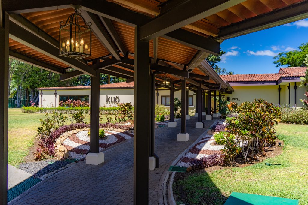 A rustic, wooden-beamed outdoor corridor with views of the surrounding green landscapes and circular stone-lined flower beds.
