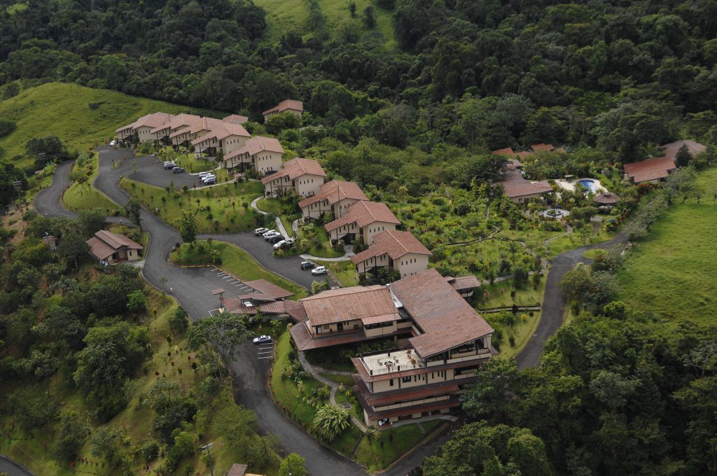 A high-angle aerial view showing rows of luxury suites nestled into the dense tropical greenery of the 27-acre property.