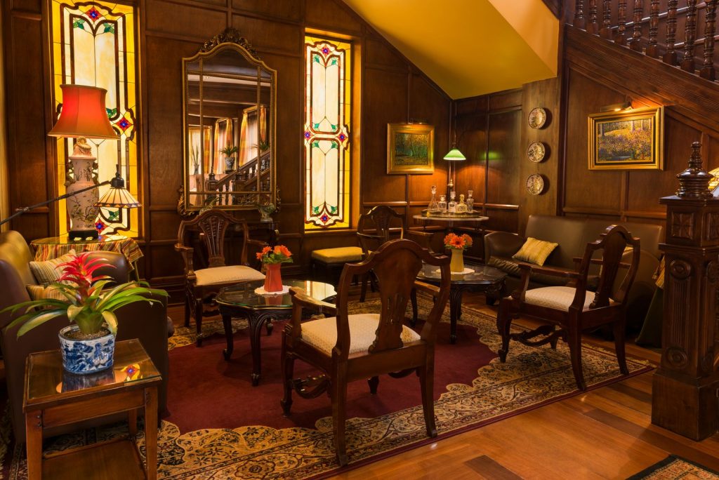 A sophisticated indoor lounge area with antique-style furniture, stained glass windows, and warm, inviting lighting.