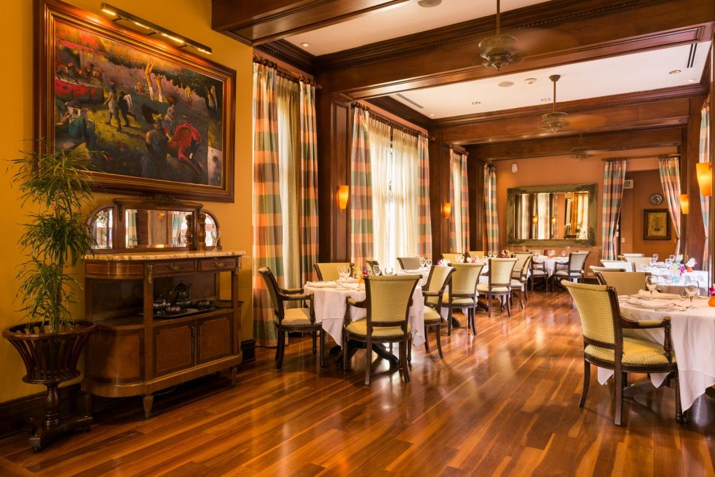 The hotel’s formal dining room showcasing polished wooden floors, classic decor, and tables dressed in white linens.