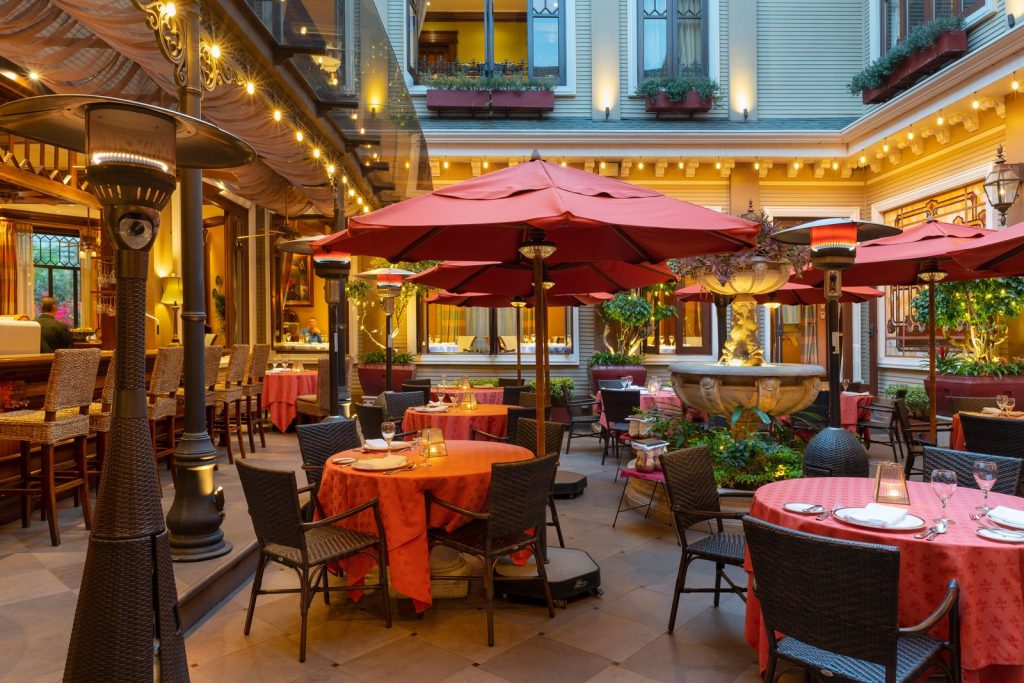 Elegant outdoor patio dining area featuring red umbrellas and neatly set tables in a charming courtyard setting.