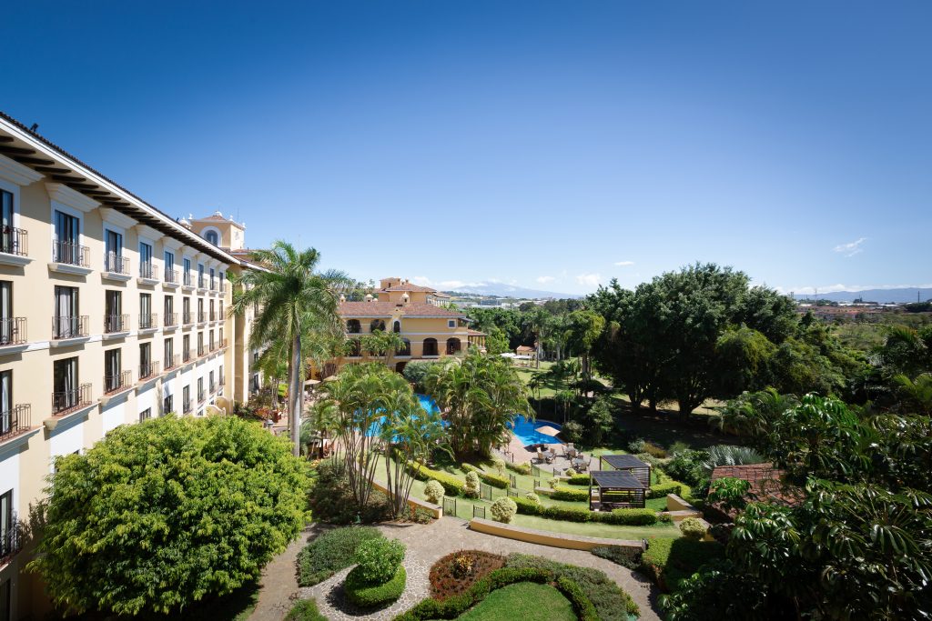 An elevated view of the lush, manicured tropical gardens and walking paths connecting the different wings of the hotel under a clear blue sky.