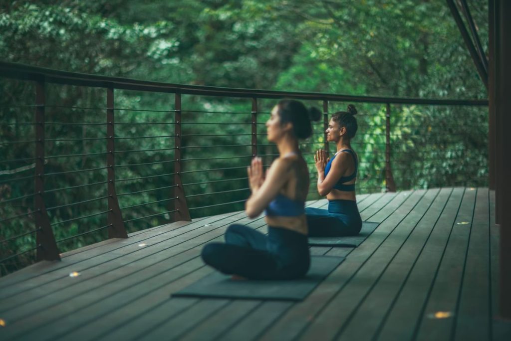 Two guests practicing yoga on a private wooden deck overlooking the vibrant green cloud forest at El Silencio