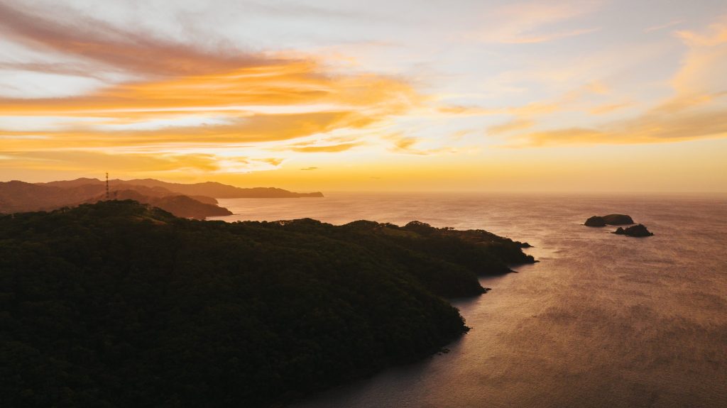 golden sunset over a mountainous coastline with small islands in the distance, with the sky filled with vibrant orange and yellow clouds