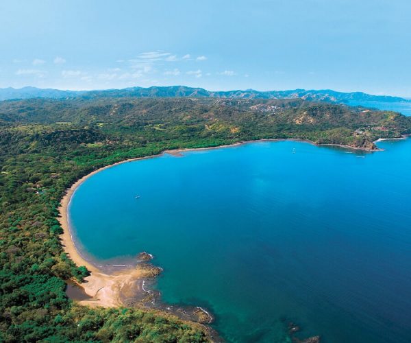 A serene sandy beach in Guanacaste with sailboats and catamarans anchored in the calm blue water, a perfect setting for a private coastal tour with Horizontes Nature Experiences.