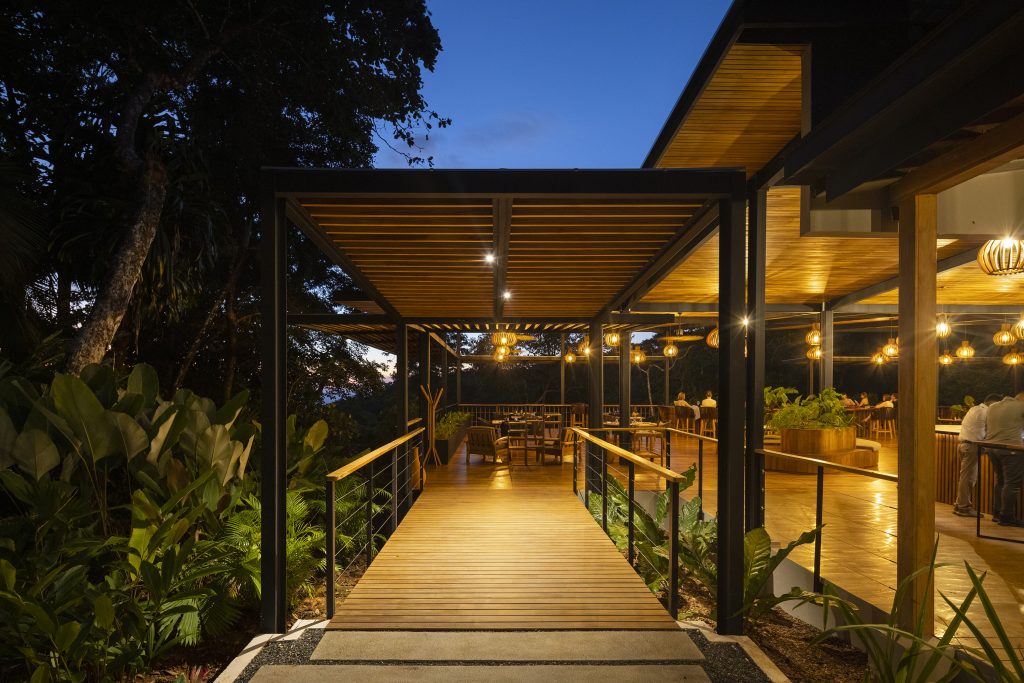 Modern glass-walled lodge building with white stone paths at El Remanso, surrounded by tropical landscaping.