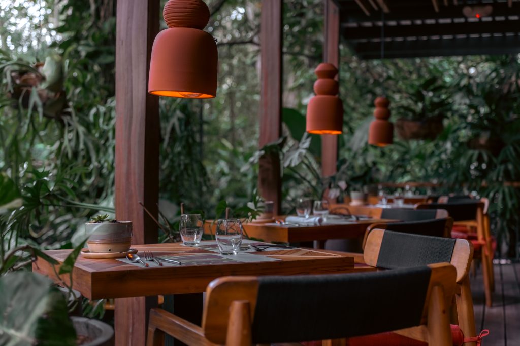 Outdoor dining terrace at Awā Beachfront Hotel with a lush rainforest backdrop and elegant clay lamps.